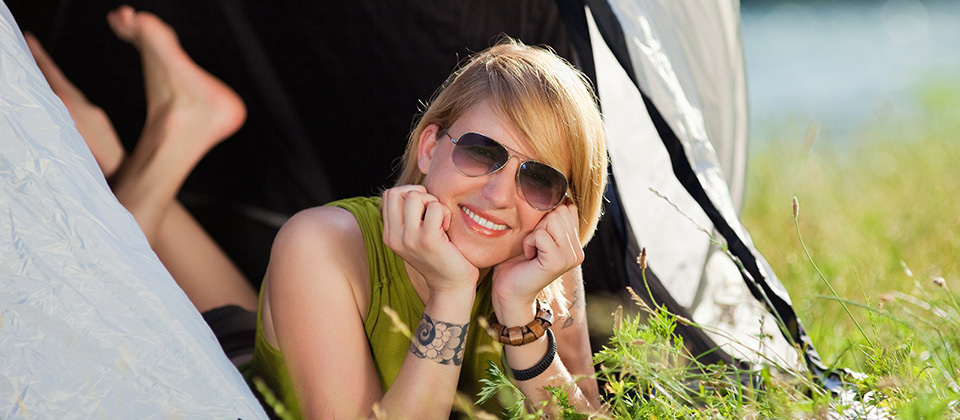 Eine lachende Frau mit Sonnenbrille, die sich in ihrem Zelt entspannt